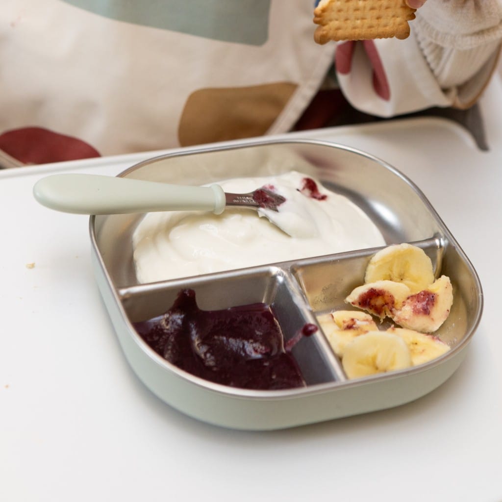 Misty Green Beaba divided plate holding fruit and yoghurt during a child's meal