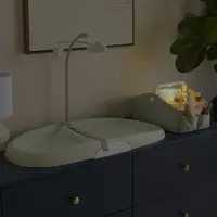 Skip Hop Sage Light Up Nappy Caddy Night Time Changing Station Illuminated Sage nappy caddy beside a change mat in a dim nursery