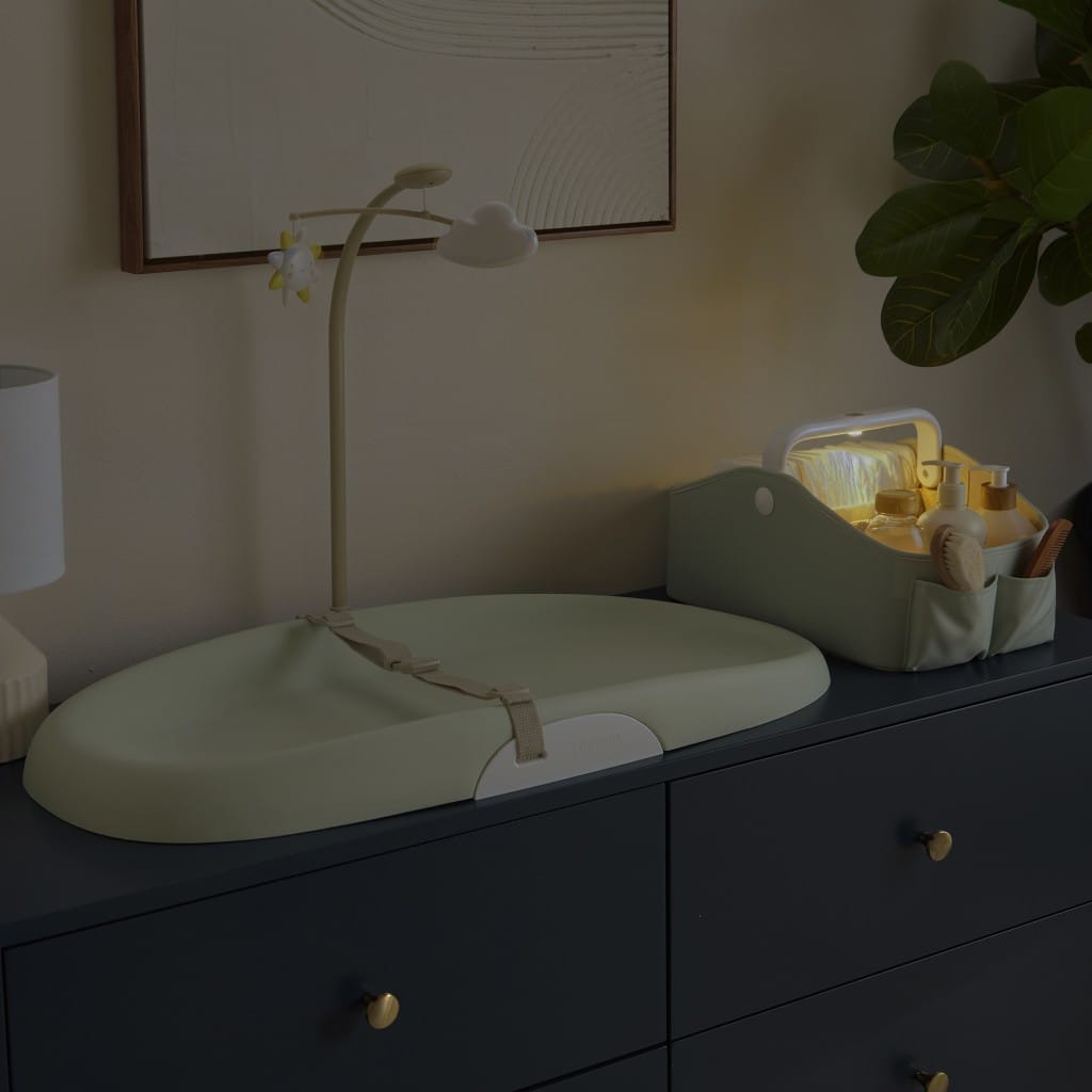 Illuminated Sage nappy caddy beside a change mat in a dim nursery
